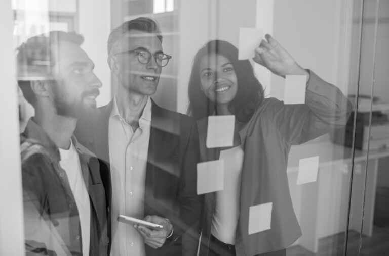 People putting sticky notes on a transparent white board